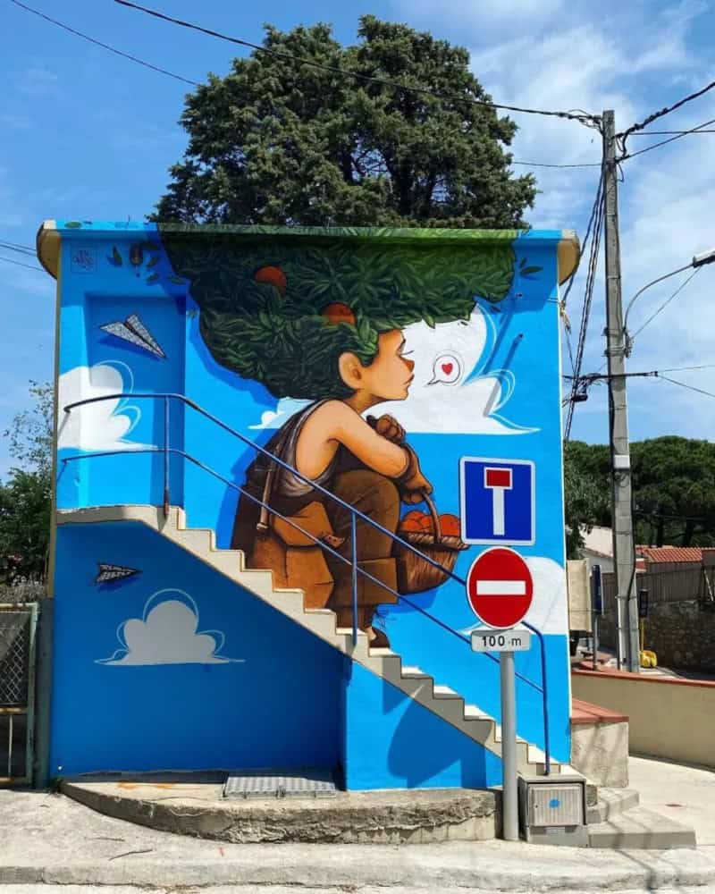 Mural of a girl with green hair sitting on stairs, with a blue sky and clouds background.