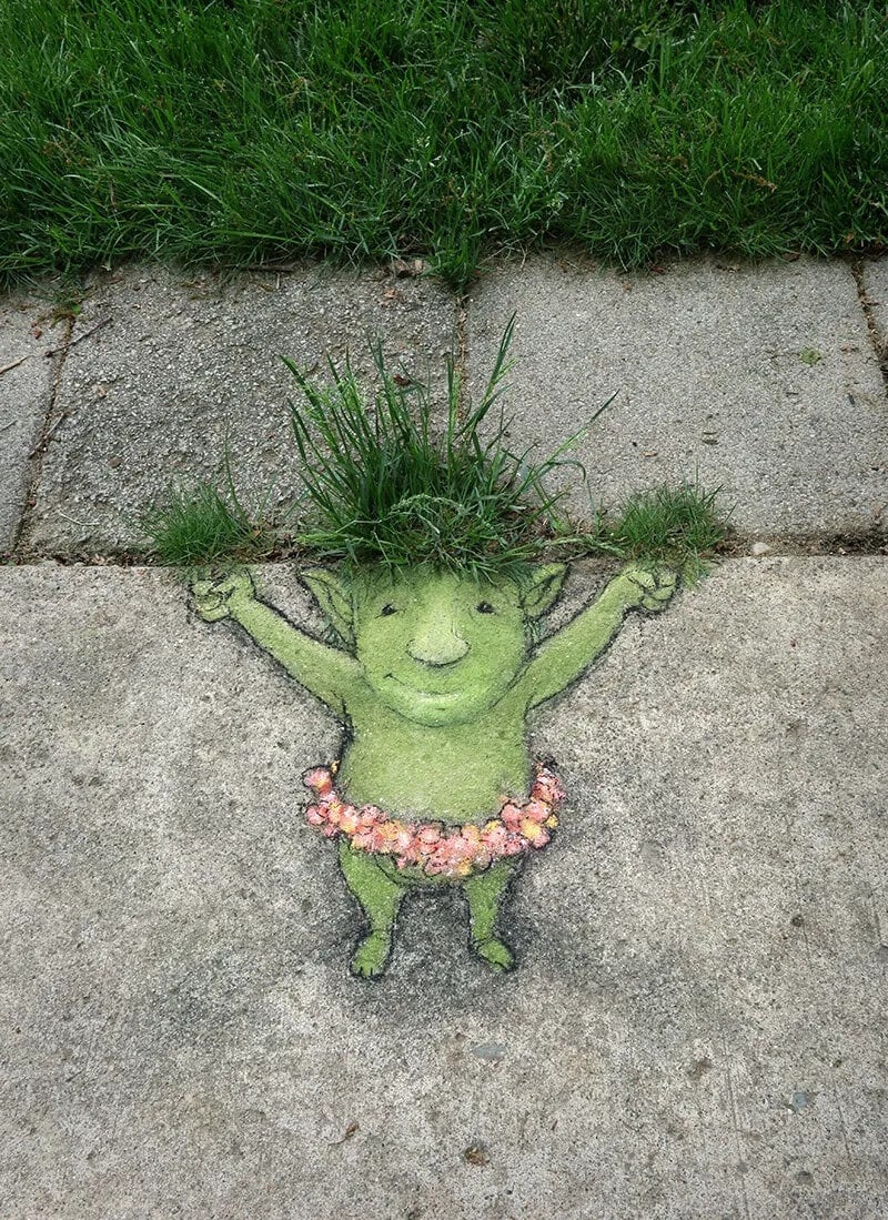 Whimsical sidewalk art of a green creature with grass hair and a flower necklace.