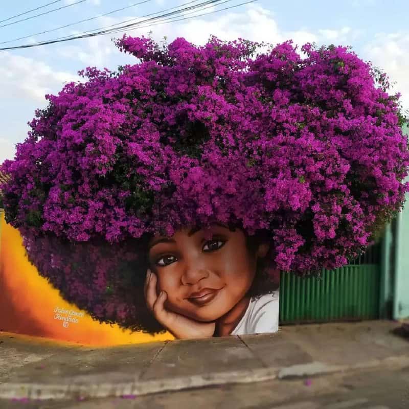 Woman with large purple flower-shaped hair mural on wall.