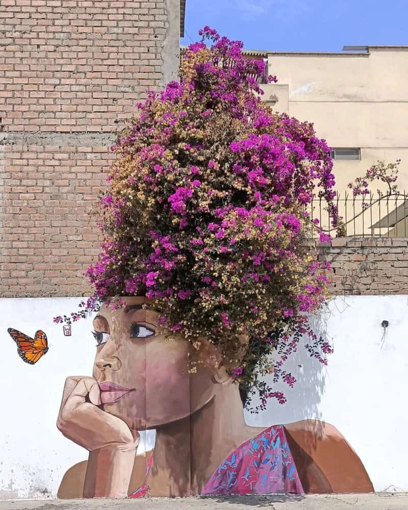 A woman with a large, vibrant bougainvillea flower crown on her head, painted on a wall.