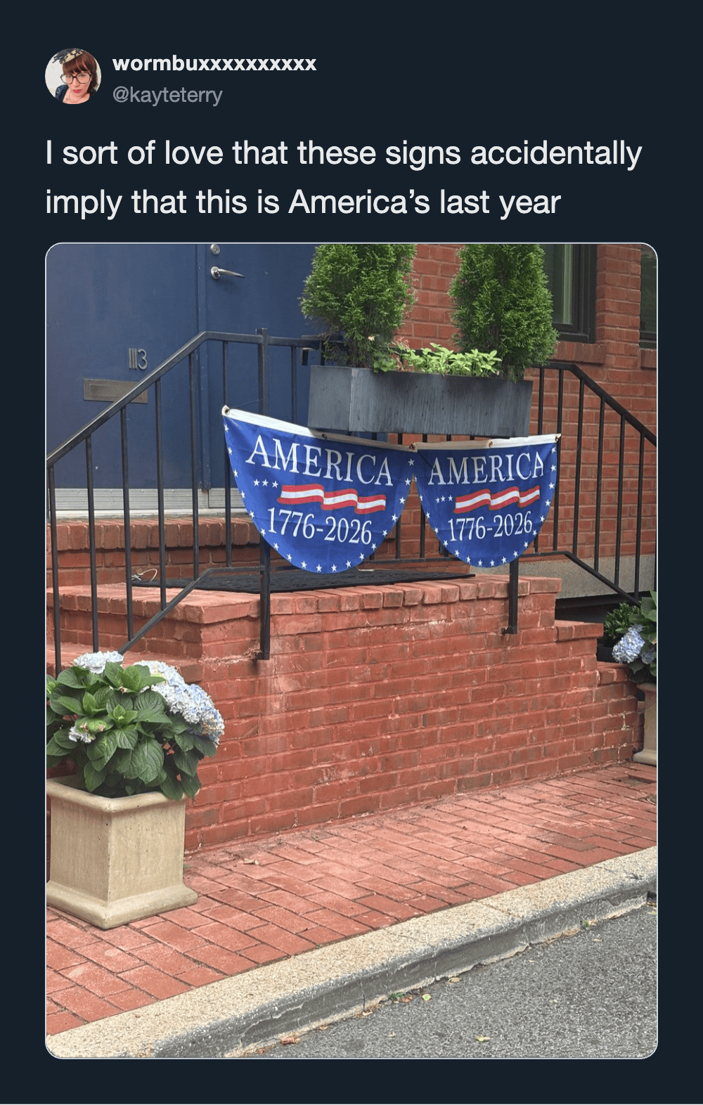 "America 1776-2026 banner hanging on a brick porch railing with plants and flowers nearby".