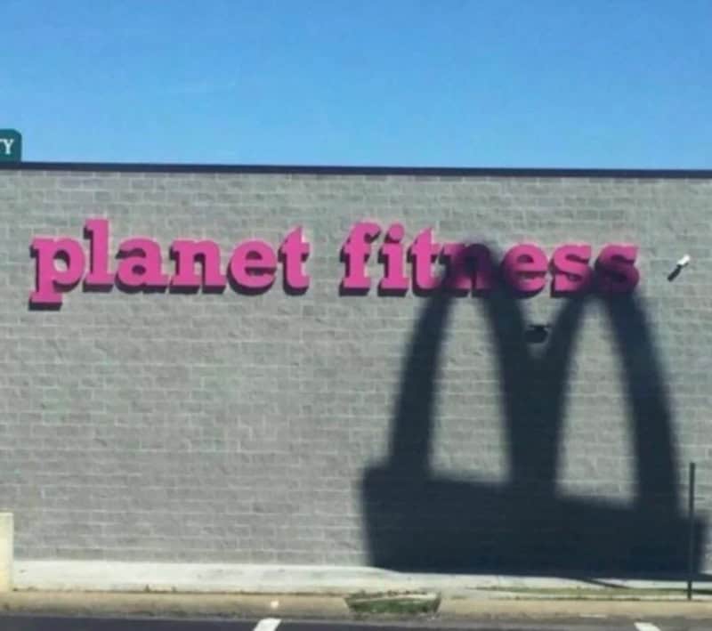 Planet fitness sign on a brick wall with shadow of a McDonald's logo.