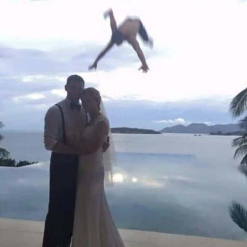 A woman in a wedding dress and a man in formal attire standing by the water with a flying horse in t.