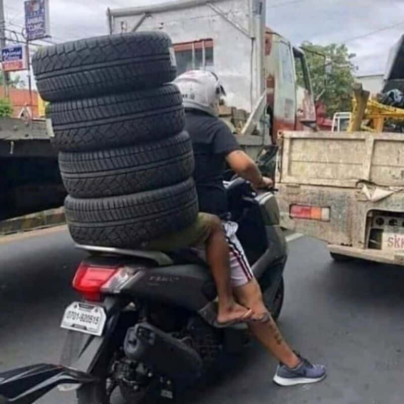 Tire stacked on motorcycle with a person riding on a busy road.
