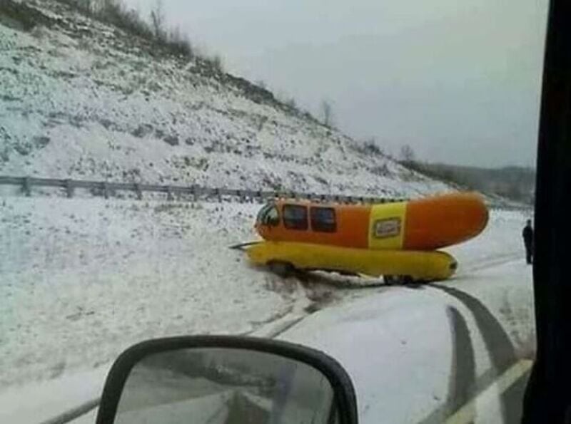 A snow-covered road with a yellow and orange helicopter stranded in the snow.