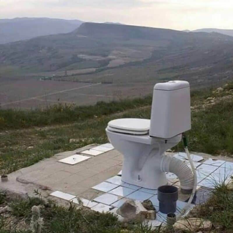 Toilet outdoors on a hillside with scenic landscape in the background.