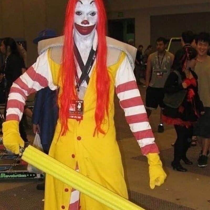 A1: Cosplayer dressed as Pennywise from It with a yellow dress and red hair at a convention.