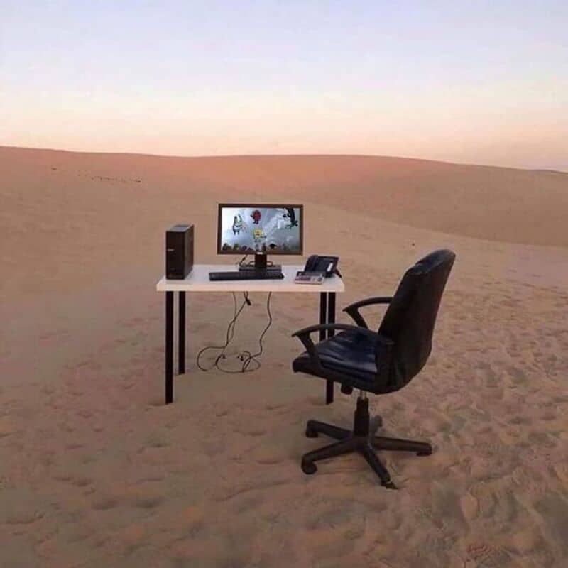 Office setup with computer and chair in desert landscape at sunset.