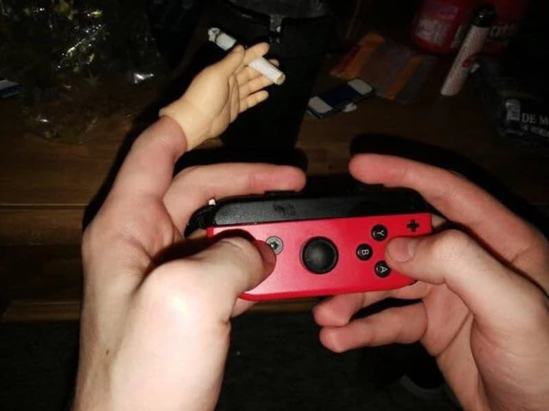 A handheld gaming console being held by two hands, with a small white object in the background.