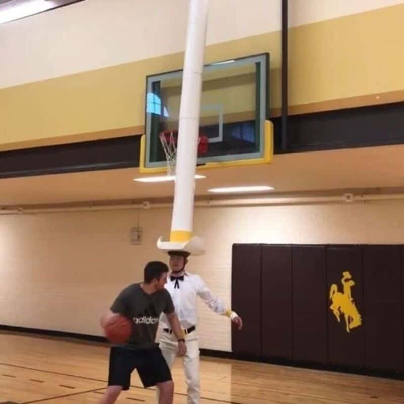Person with a basketball and a person in a cowboy costume in a gymnasium.