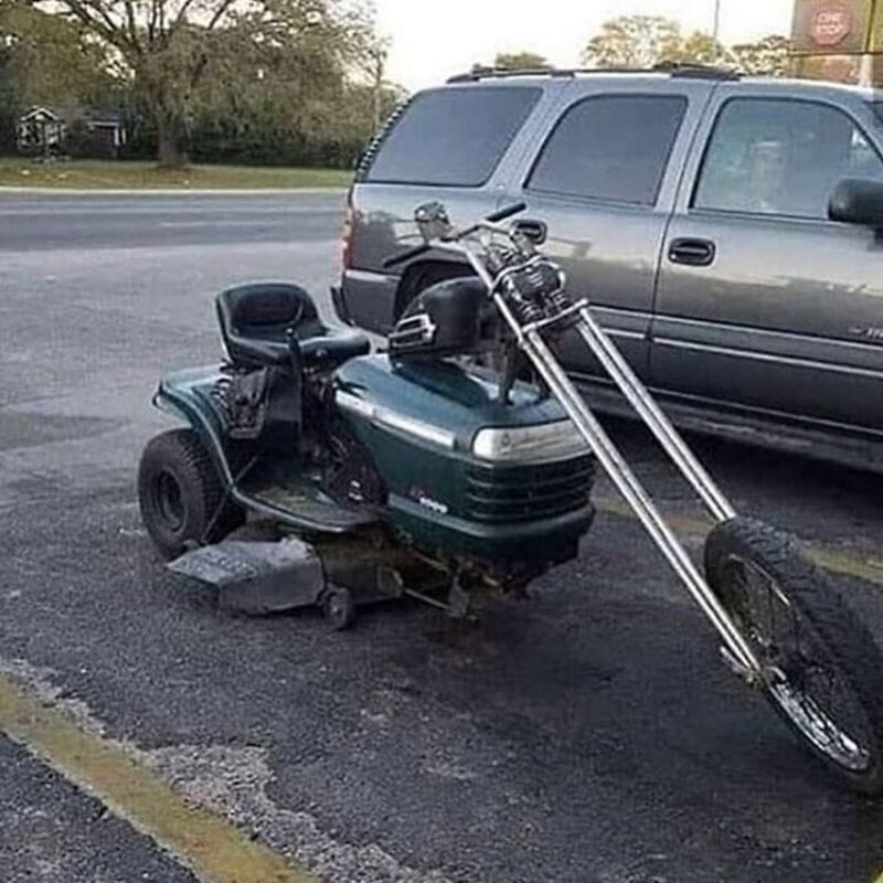 Modified lawn mower with motorcycle front fork in parking lot.
