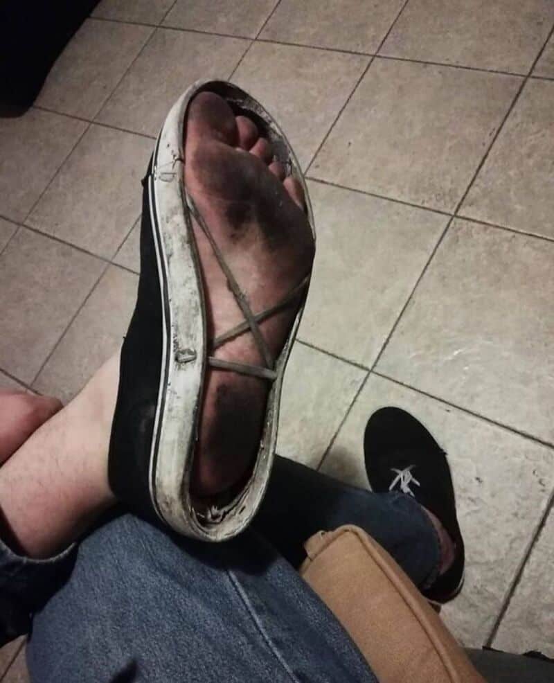 Dirty, worn-out sandal with a black strap and white sole on a tiled floor.