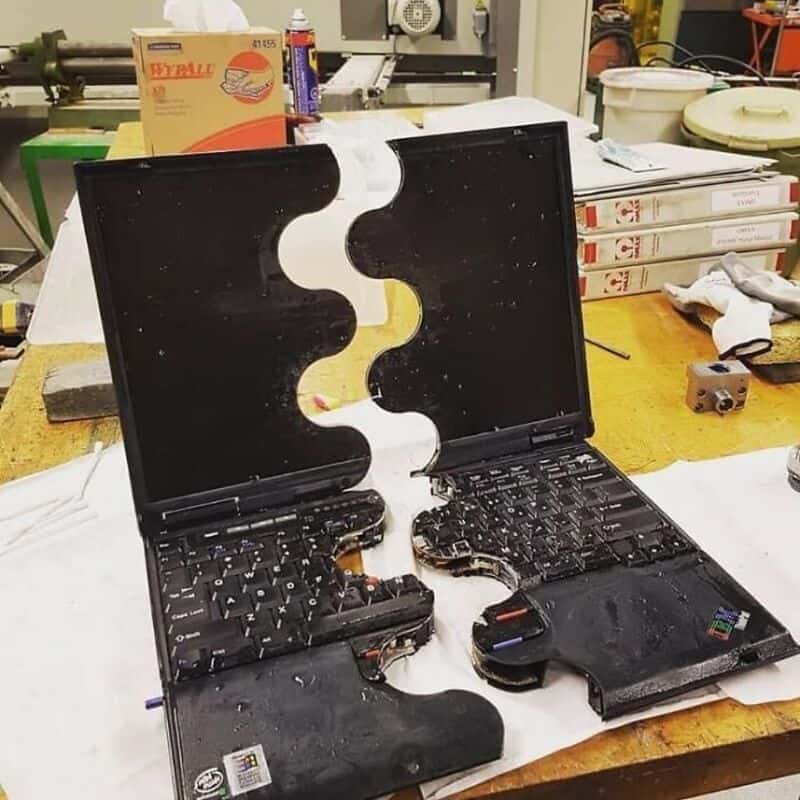 Broken laptop with mirror reflection on a cluttered workbench.