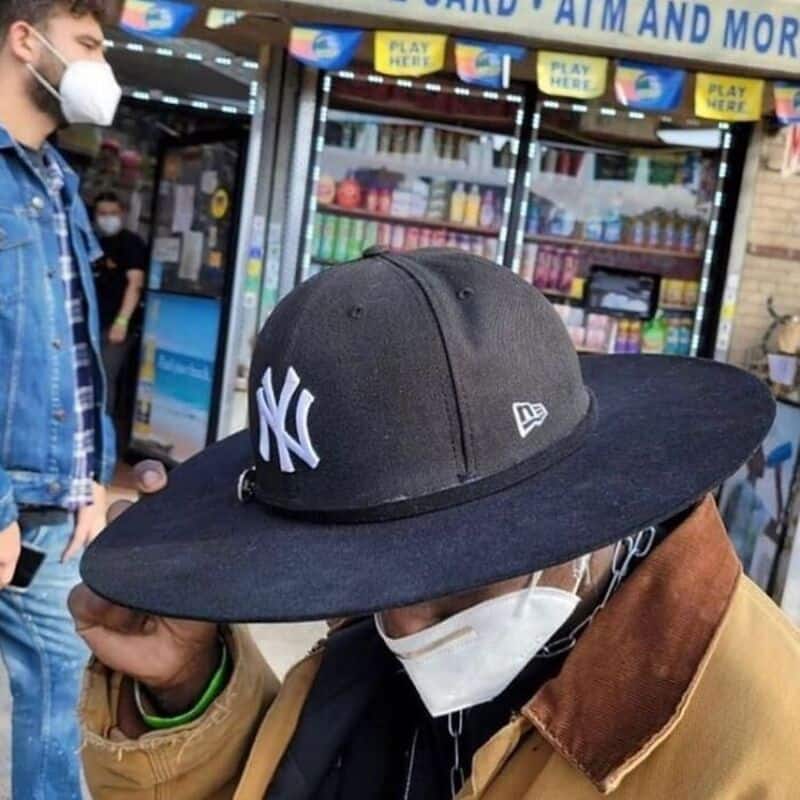 NY Yankees baseball cap worn by a person in a mask at a store entrance.