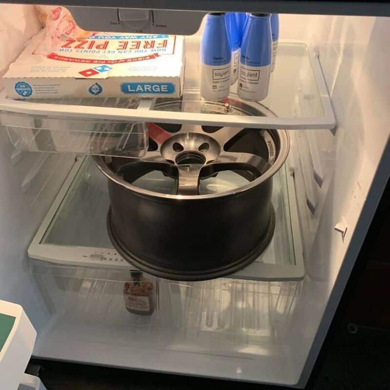 Car wheel inside a refrigerator with cleaning supplies on top shelf.