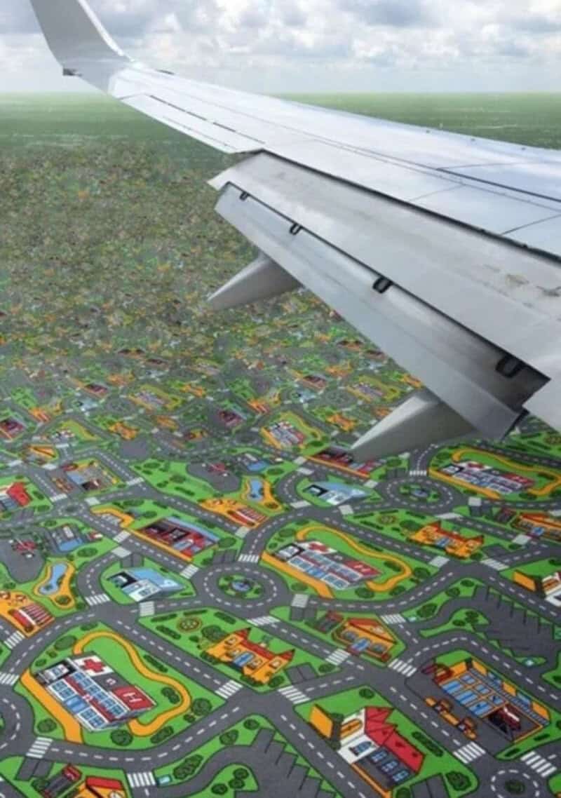 Airplane wing flying over a colorful miniature cityscape.
