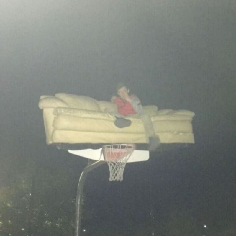 A young girl sitting on a sofa that is floating above a basketball hoop at night.
