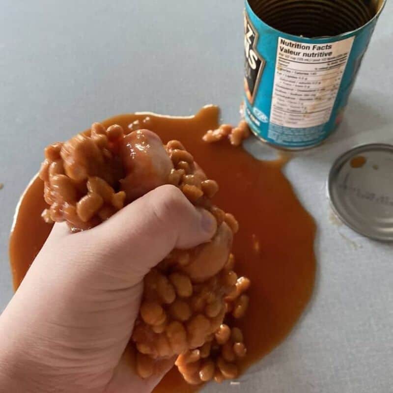 Hand squeezing caramel from a can with spilled caramel on table.