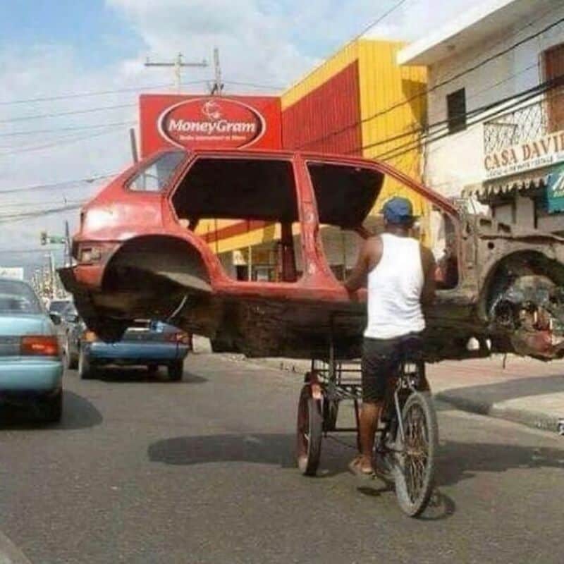 Man riding a bicycle with a car body on a street.