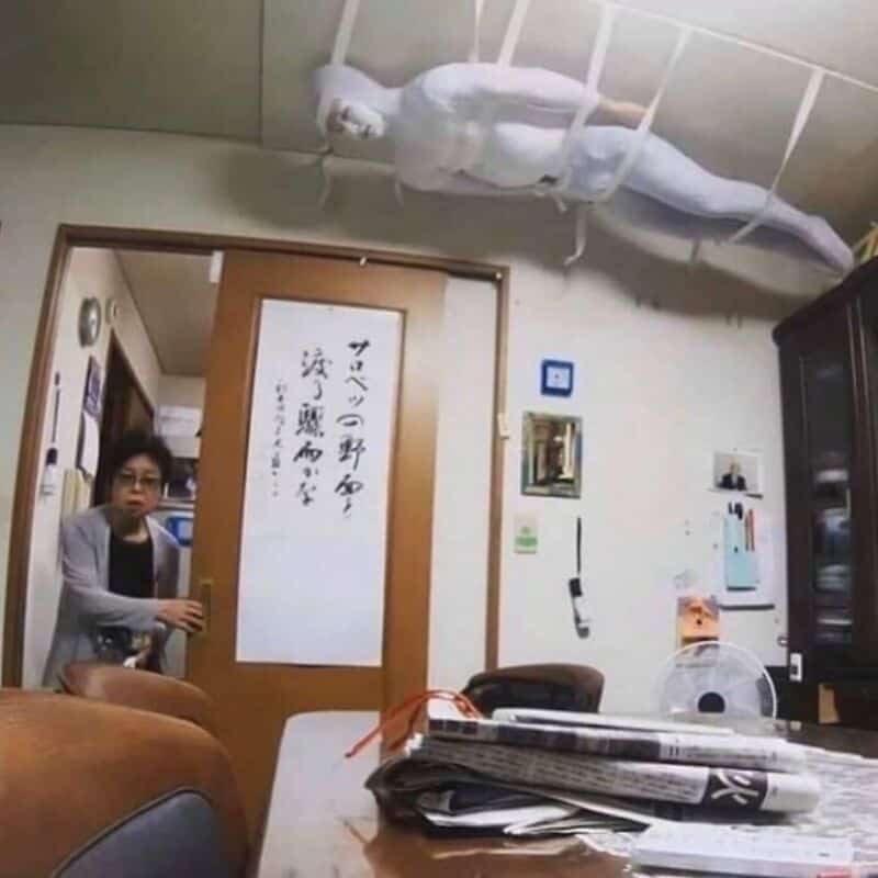 A woman sitting at a table with a large white lizard hanging from the ceiling.