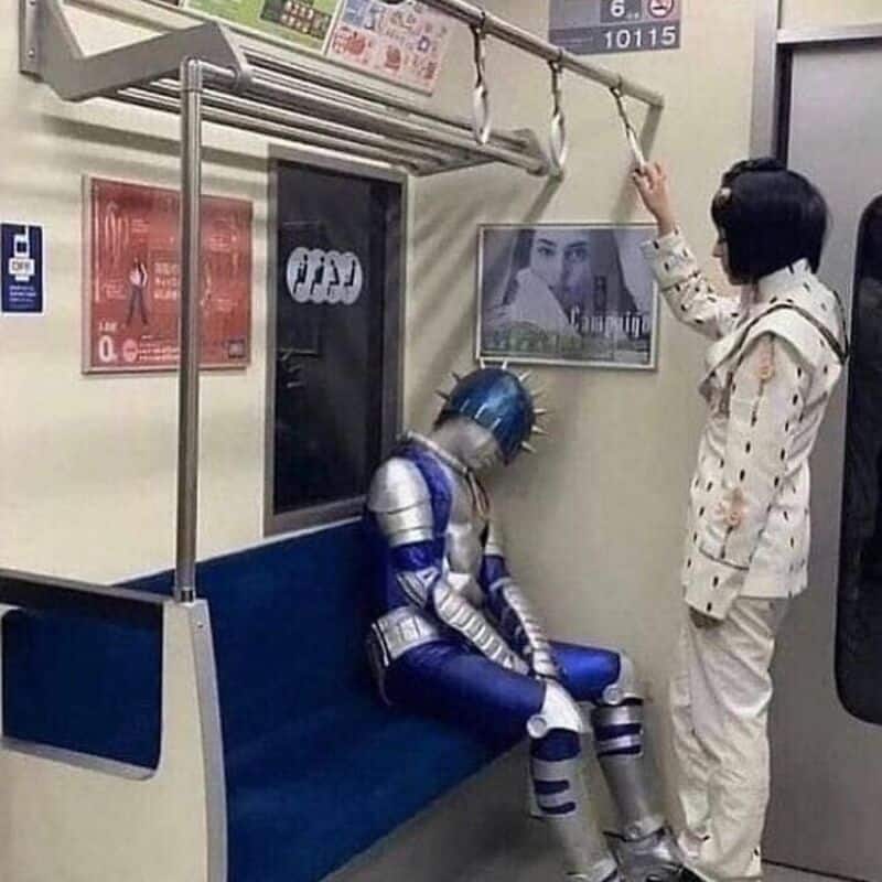 A woman standing in a subway train, reaching for a handrail, while a person dressed in a futuristic.