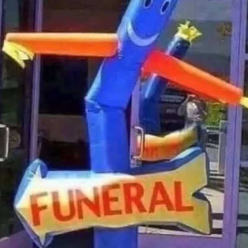 Funeral sign with a smiling blue character and orange arms, pointing to the entrance.