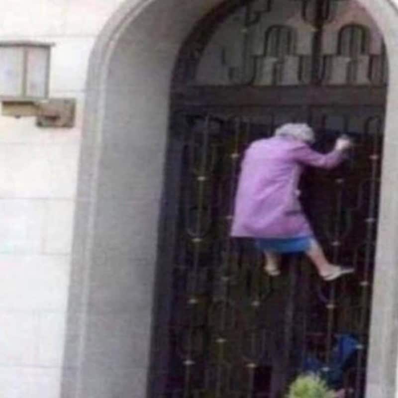 A woman in a purple coat climbing a dark gate outside a building.