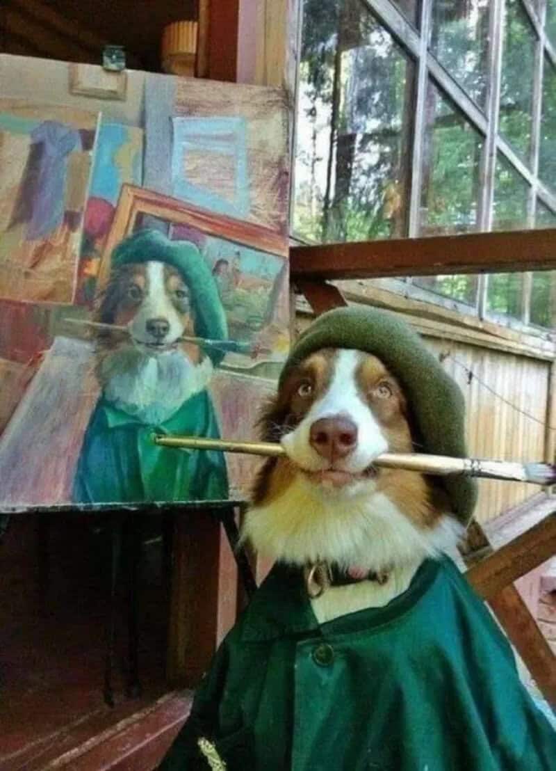 Dog dressed as an artist with a paintbrush in mouth and a hat, in front of a painting.