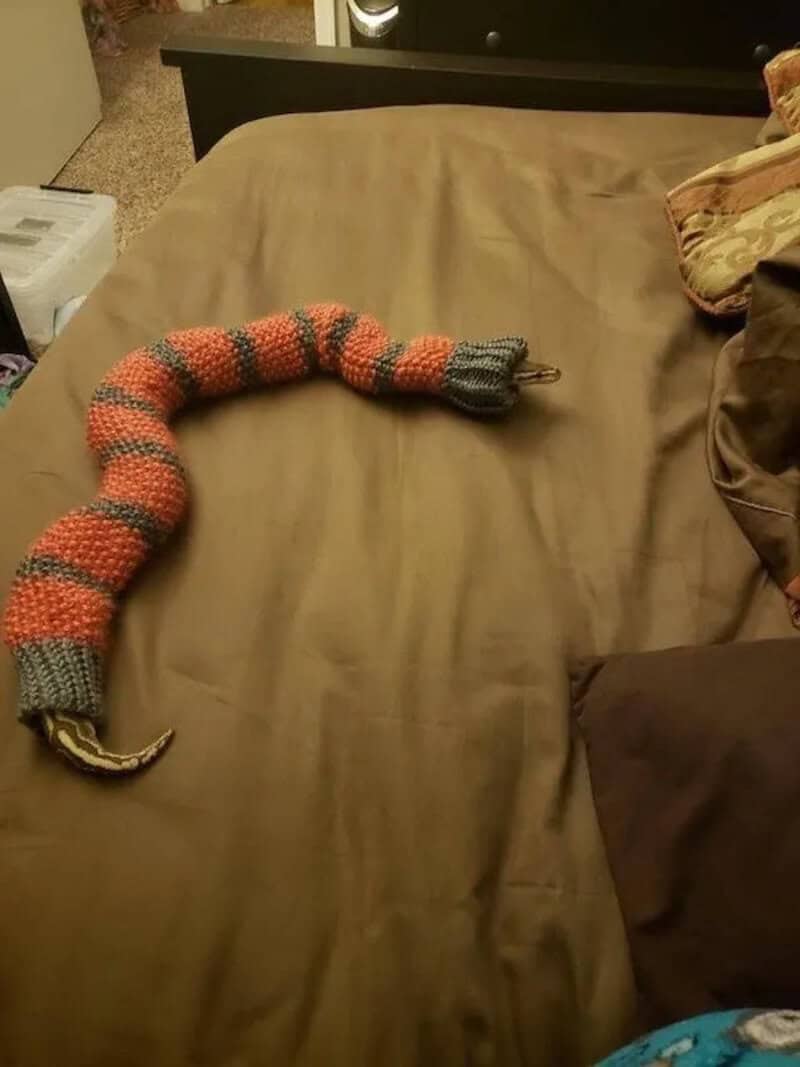 Knitted snake toy on bed with brown sheets and pillows.