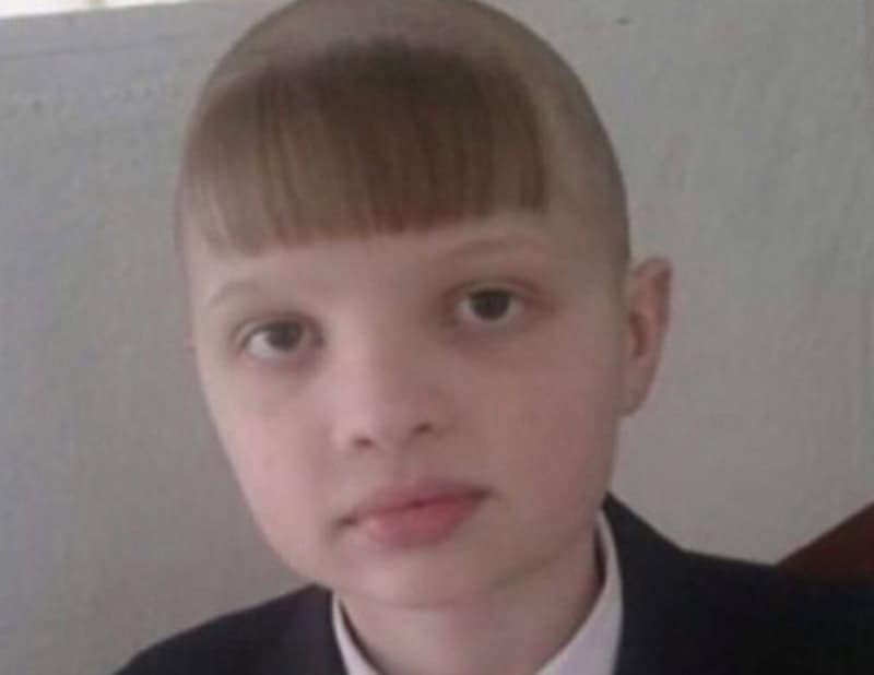Child with uneven haircut and a serious expression, wearing a dark jacket.