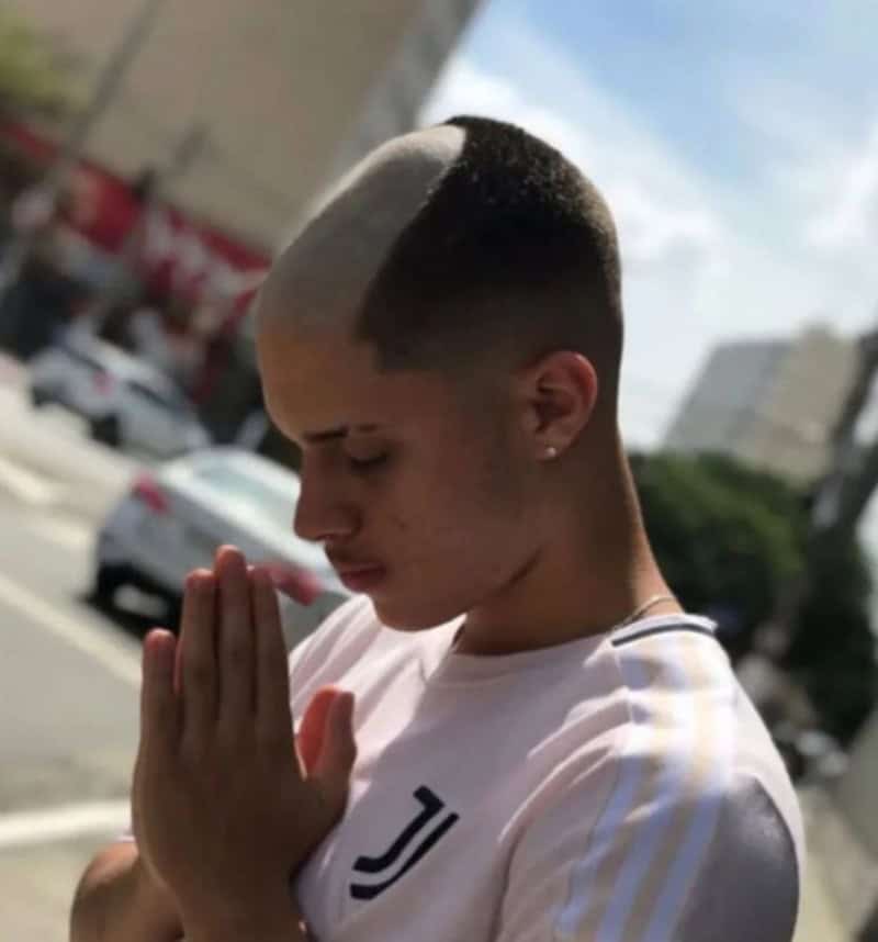 Young man with a unique haircut praying outdoors, with a large gray streak in his hair.
