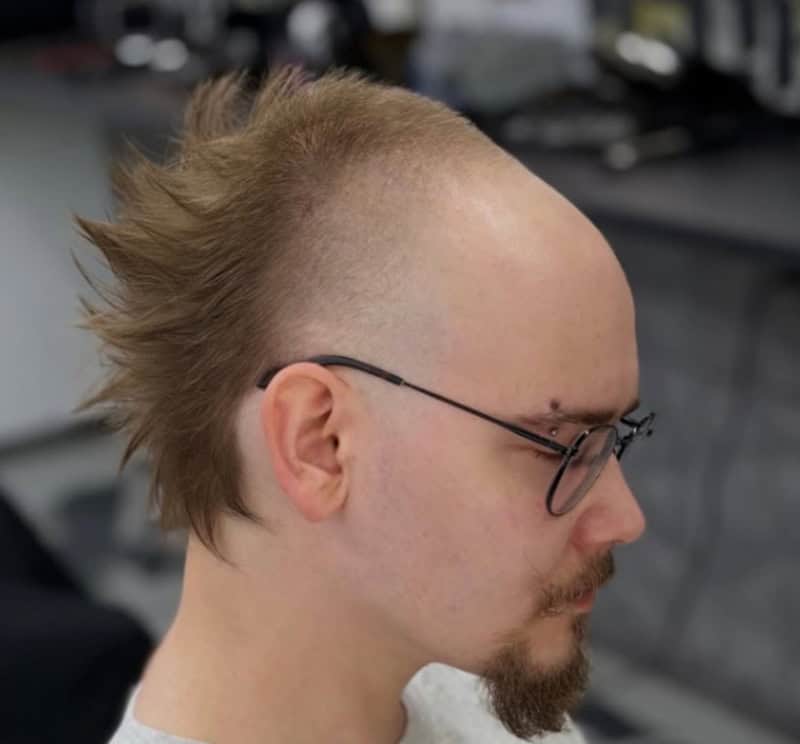Side view of a man with a mohawk hairstyle and glasses in a barbershop.