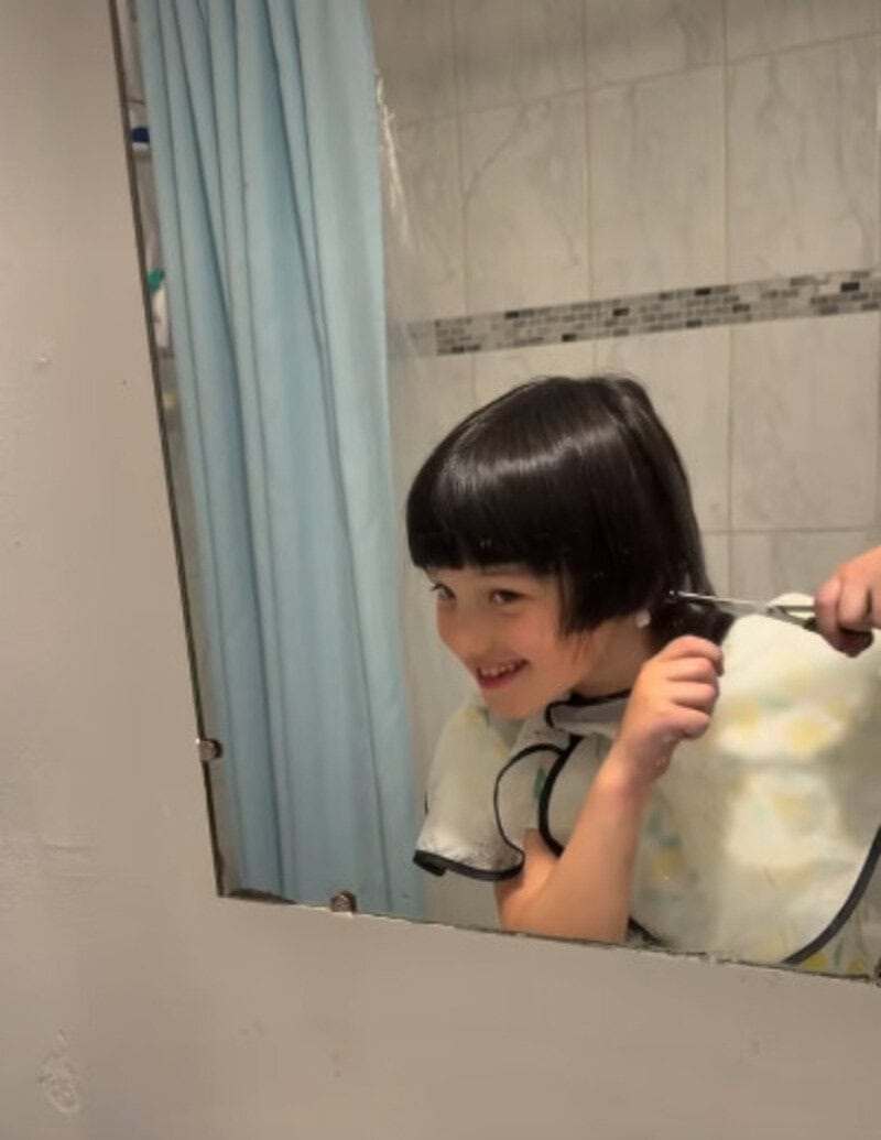 Child with a funny haircut smiling in a mirror during a haircut fail.