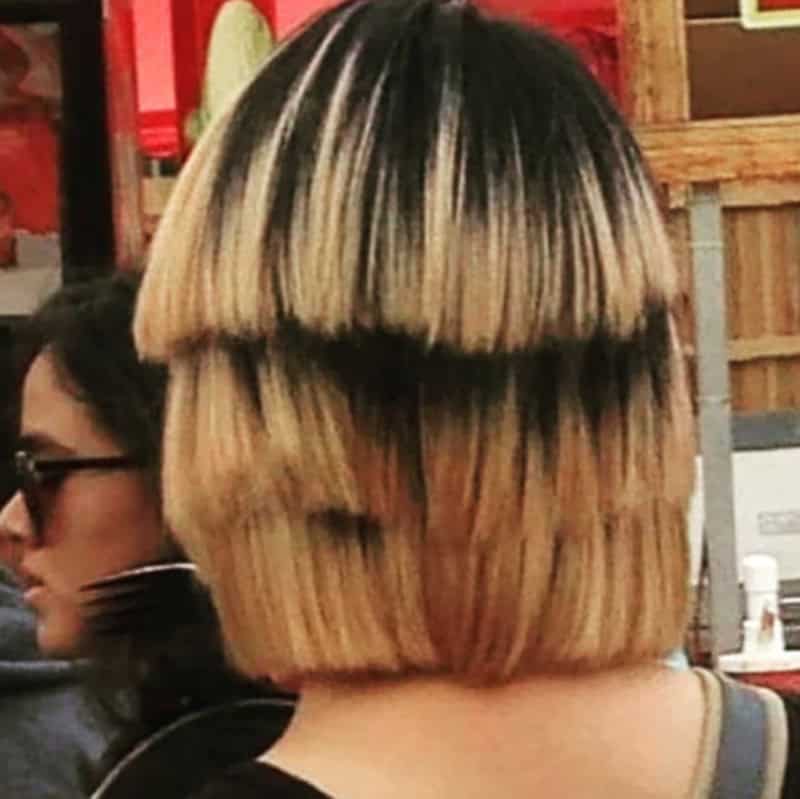 Back view of a woman with a poorly cut blonde bob hairstyle with uneven layers.