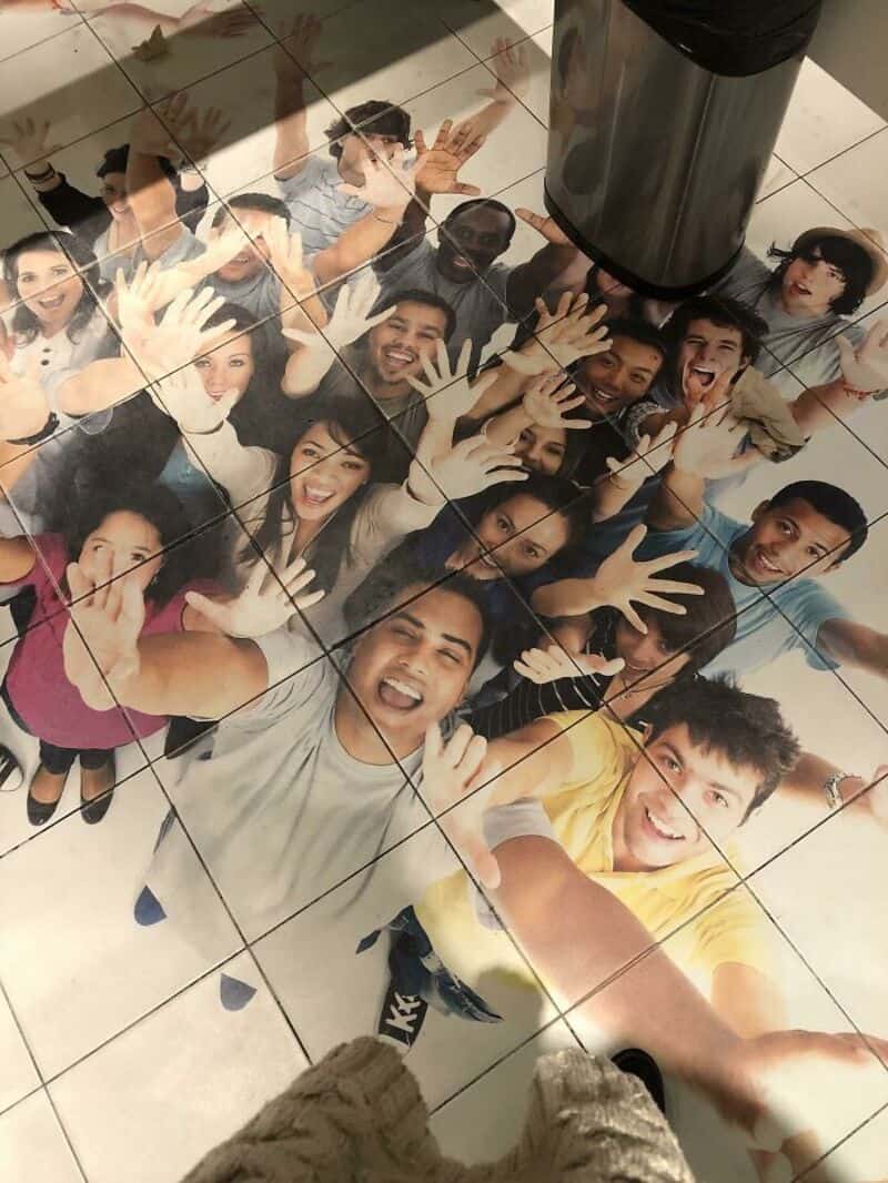 Group of people taking a selfie from above, smiling and waving at the camera.