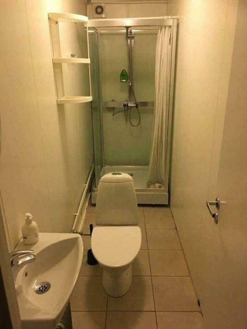 Small bathroom with shower, toilet, and sink in a narrow space.