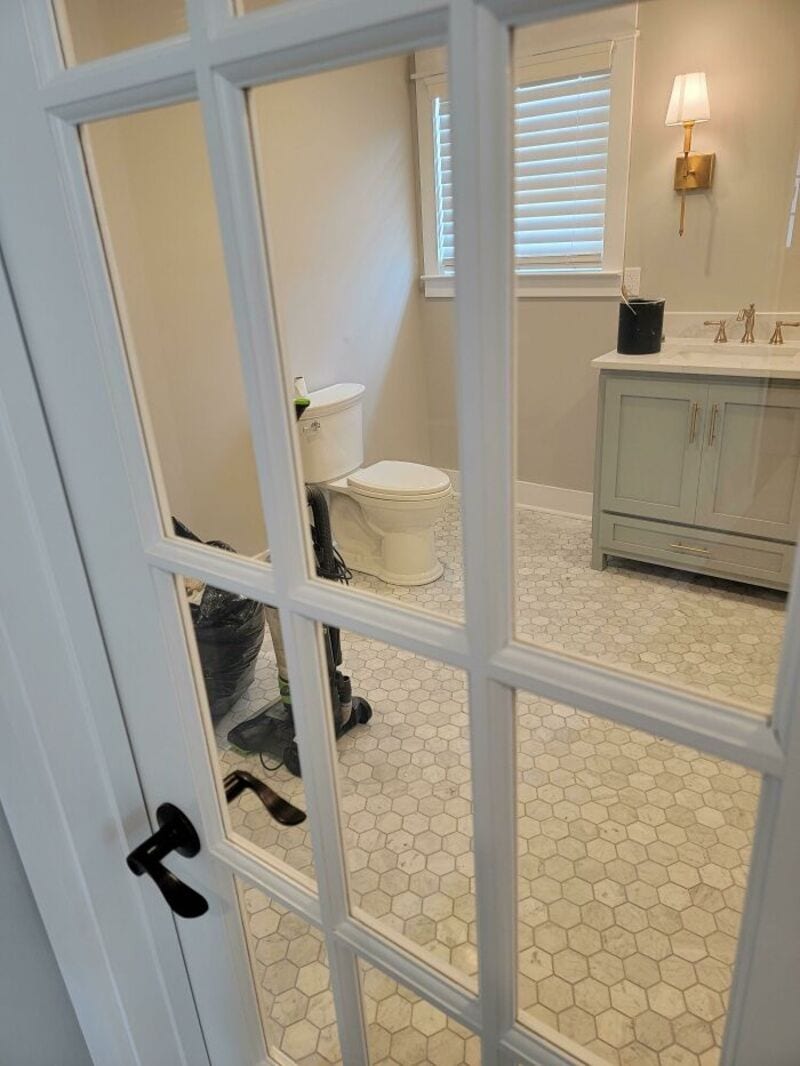 Bathroom with toilet and vanity, viewed through a glass door.
