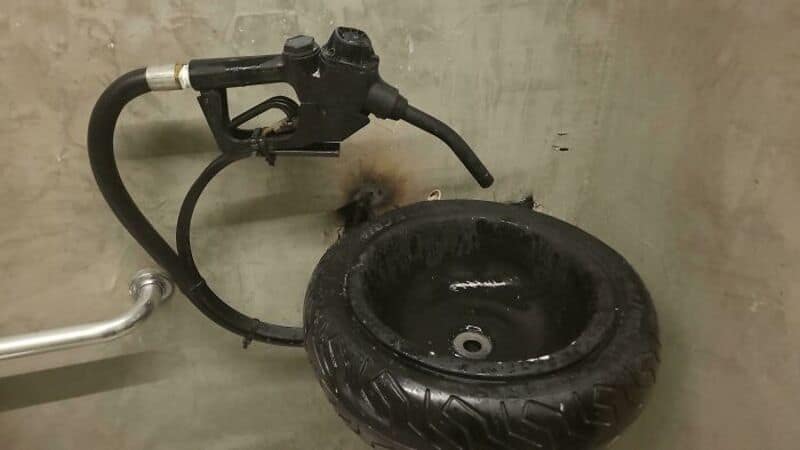 A small sink with a tire as the basin and a faucet attached to the wall.
