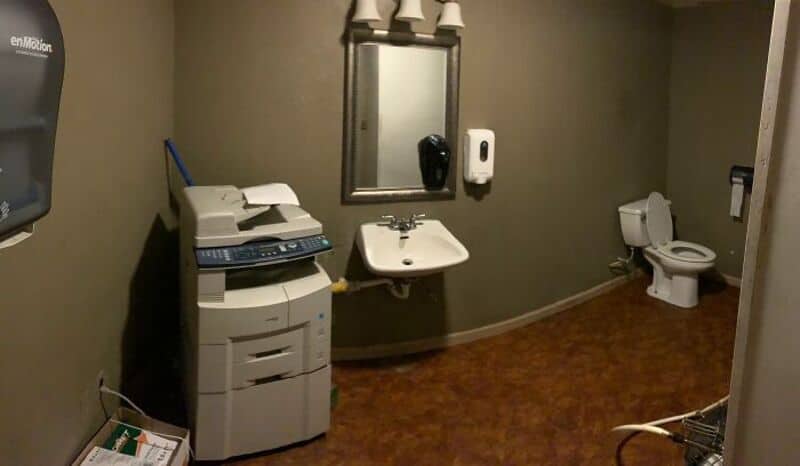 Bathroom with a sink, mirror, toilet, and a copier machine.