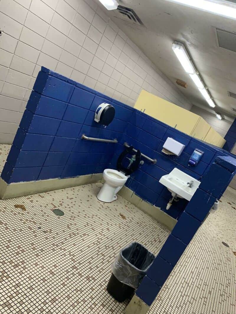 Bathroom with blue tiled wall, toilet, sink, and trash can, in a poorly maintained space.