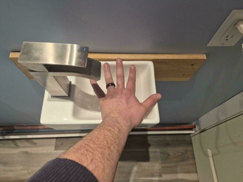 Bathroom sink with a hand in front, faucet and wooden shelf above, part of a bathroom design fail.