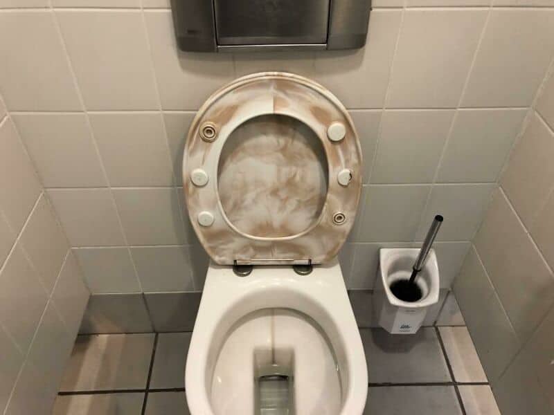 Toilet with a broken seat and a plunger nearby in a bathroom.