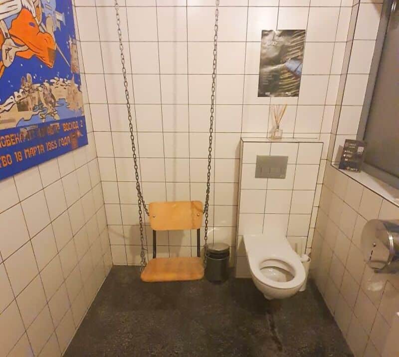 Bathroom with a swing instead of a toilet seat, tiled walls, and a poster on the wall.