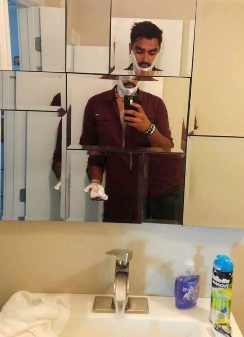 Man taking mirror selfie in bathroom with broken mirror tiles.