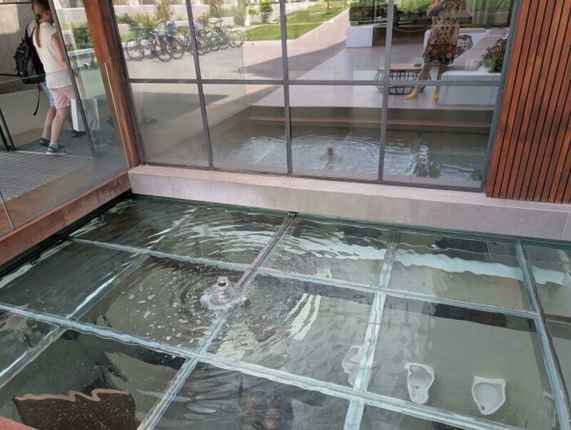 Bathroom design fail with urinals installed over a glass floor with water underneath.