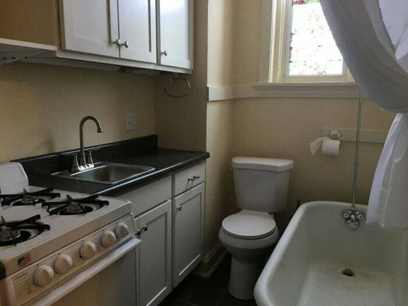 Bathroom with a kitchen sink, stove, toilet, and bathtub in a small space.