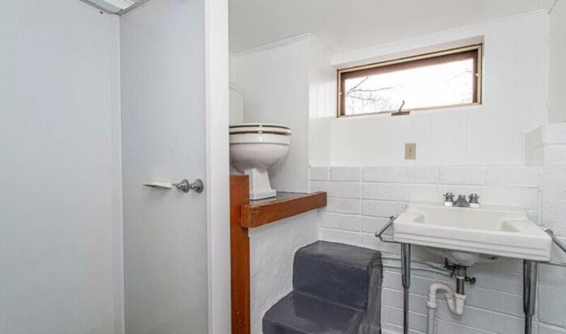 Small bathroom with a toilet, sink, and window, showing a design fail.