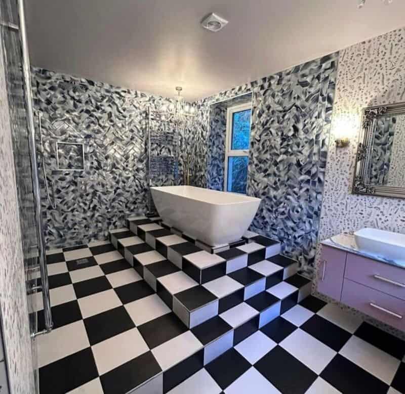 Bathroom with checkered black and white floor, patterned walls, and a bathtub on stairs.