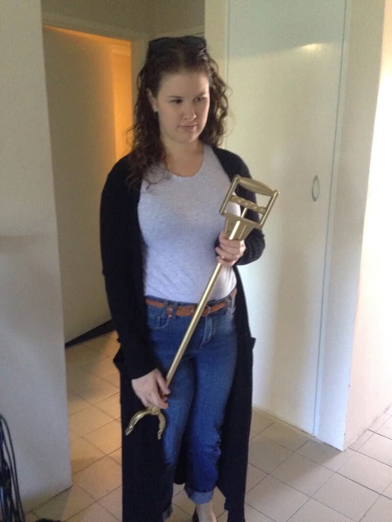 Woman holding a large gold key in a room with white walls and tiled floor.