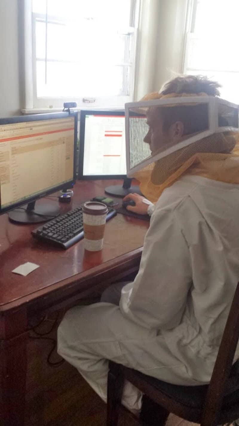 A woman wearing a protective face shield working at a desk with multiple computer monitors.